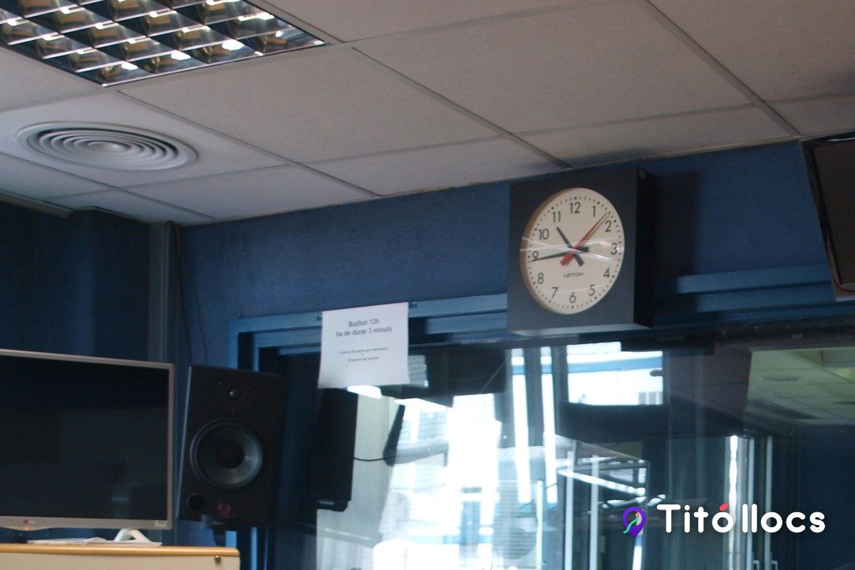 Sala de control d'un estudi de ràdio, a Catalunya Ràdio, amb monitors, altaveus i un rellotge de paret.