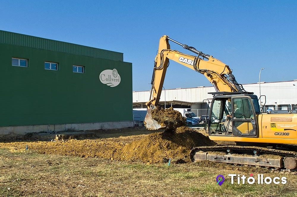 Excavadora groga treballant davant d'una nau industrial verda de Can Pipa