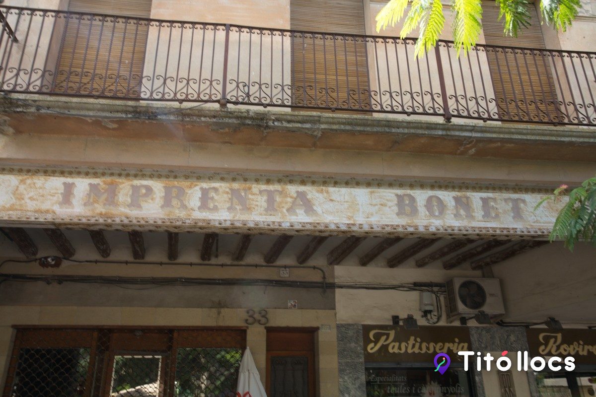 Façana porxada de la plaça Major amb el rètol antic d'Impremta Boret i, a sota, el de la Pastisseria RoviroSa