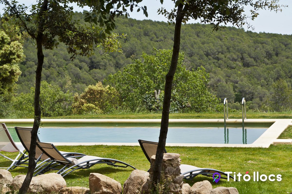 La piscina de la masia amb gandules i el bosc al fons, a Can Ros (Cistella)