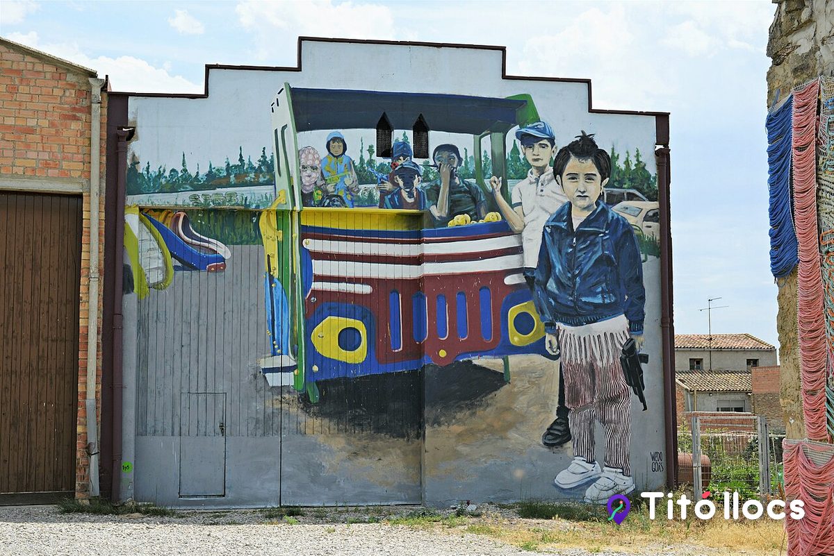 Mural d'un nen pintat al costat d'un camió de colors, a Murals de Penelles