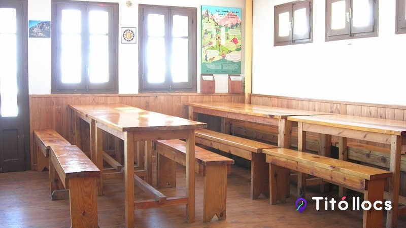 Interior del menjador del Refugi Pla de la Font, amb taules i bancs de fusta.